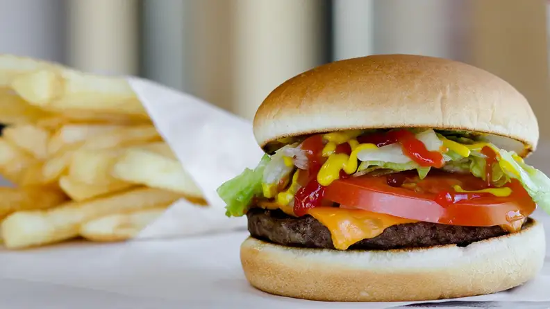 A burger sits at the forefront with French fries to the left