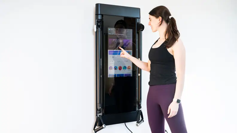 A woman selecting a workout on Tonal's touchscreen.