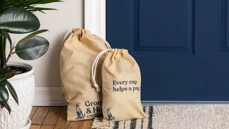 Two burlap Grounds & Hounds coffee bags by a navy blue door