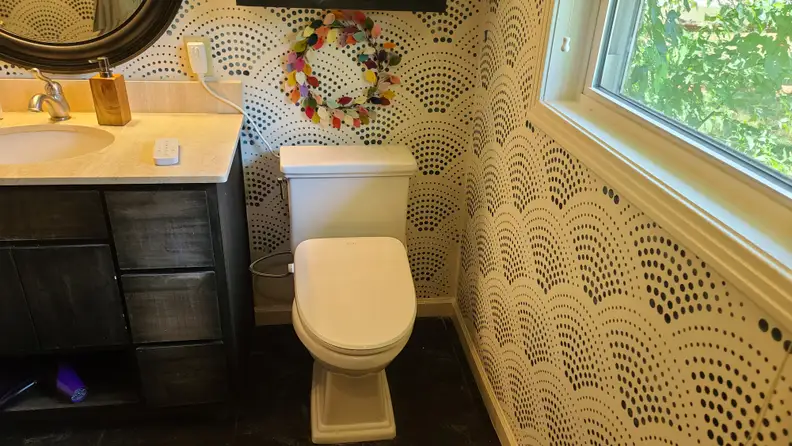 The Alpha Bidet UX Pearl installed on a toilet in a bathroom with the remote control sitting on the counter.