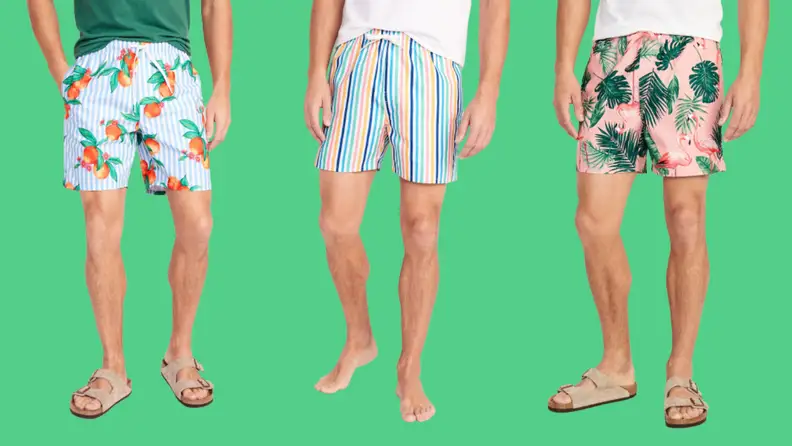 Three men's swimsuits: One with a fruit print against blue stripes, one in rainbow stripes, and one in a botanical print against a pink background.