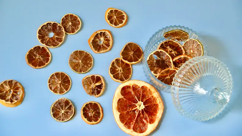 Slices of dehydrated citrus fruits are scattered around the picture and  some pieces of hydrated lime wheels are in the glass container on the right.