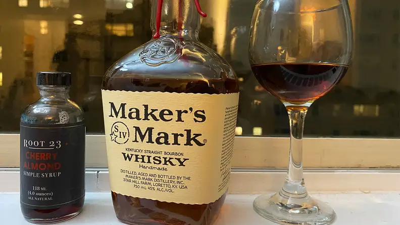 Manhattan drink next to bourbon bottle against night background