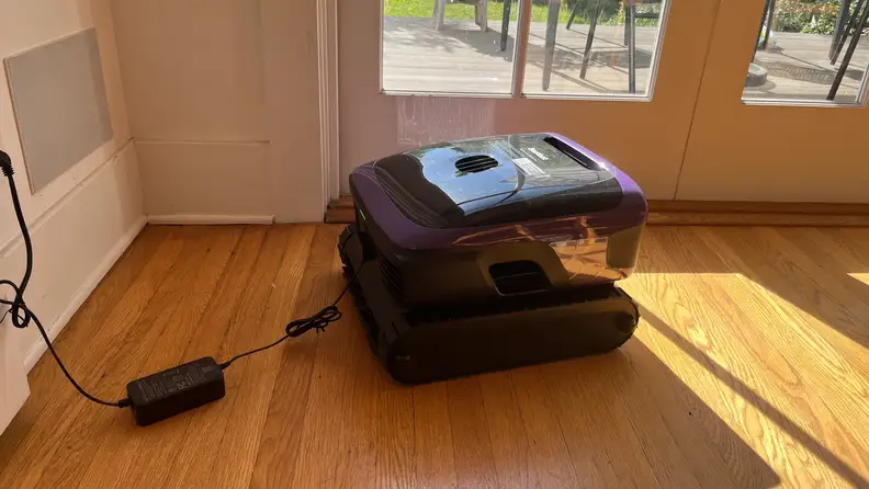 Beatbot Sora 70 pool cleaner charging, plugged into wall, sitting on a wooden floor.