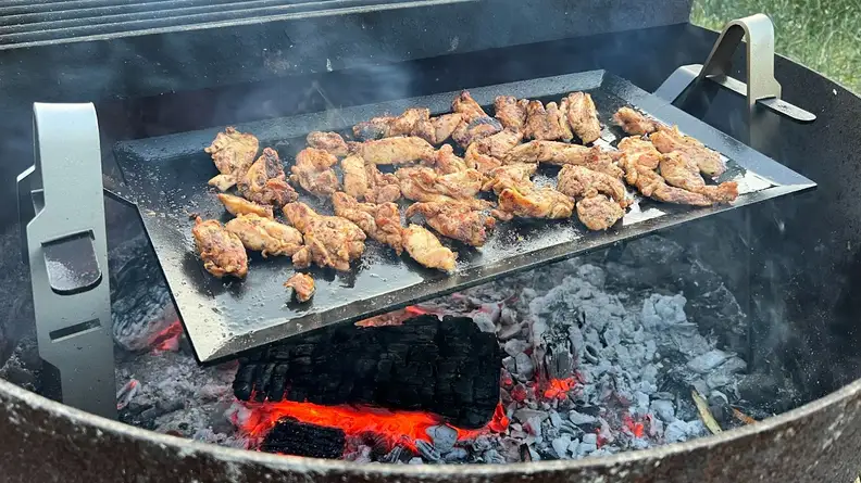 Chicken wing sections searing on top of Made In Carbon Steel Griddle cooktop inside of grill on top of hot coals.