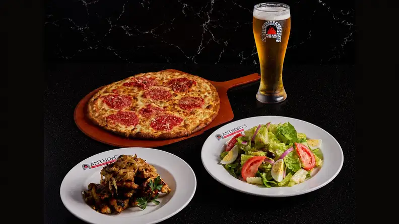 pizza, wings, salad, and a pint of beer on a table