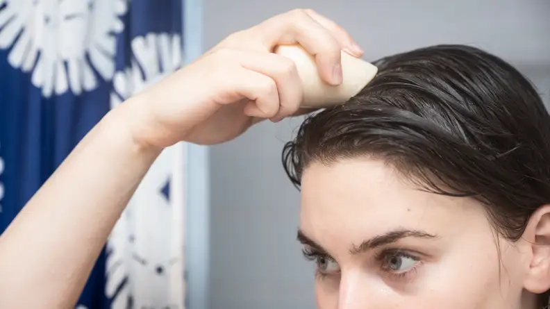 A person holding a HiBar shampoo bar to their brown hair in the shower.