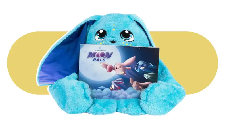 Product shot of Bo, the Moon Pal weighted stuffed animal holding a children's book.