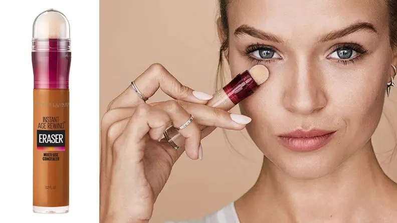 On the left: The Maybelline Instant Age Rewind Eraser Multi-Use Concealer in a tan-deep shade on a white background. On the right: A person with fair skin holds the Maybelline concealer up to their under-eyes and looks at the camera.