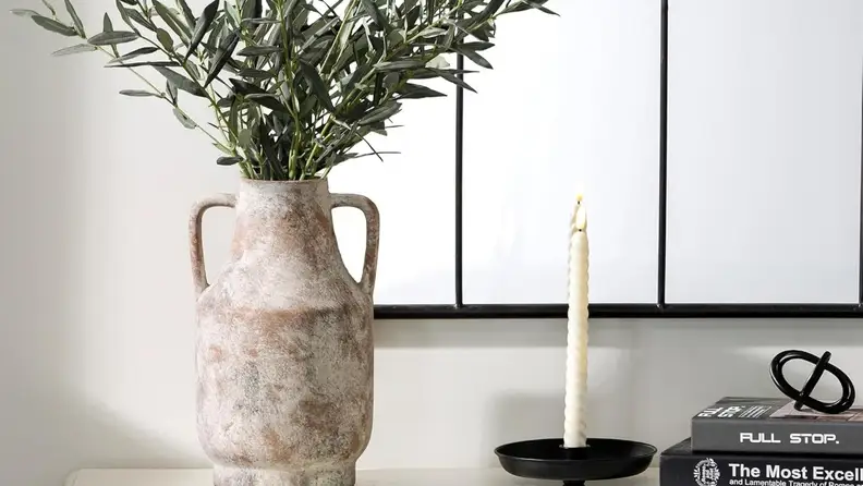 A terracotta vase filled with greenery sits in front of white artwork next to decorative books