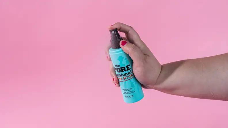 A person's hand spraying a makeup setting spray.