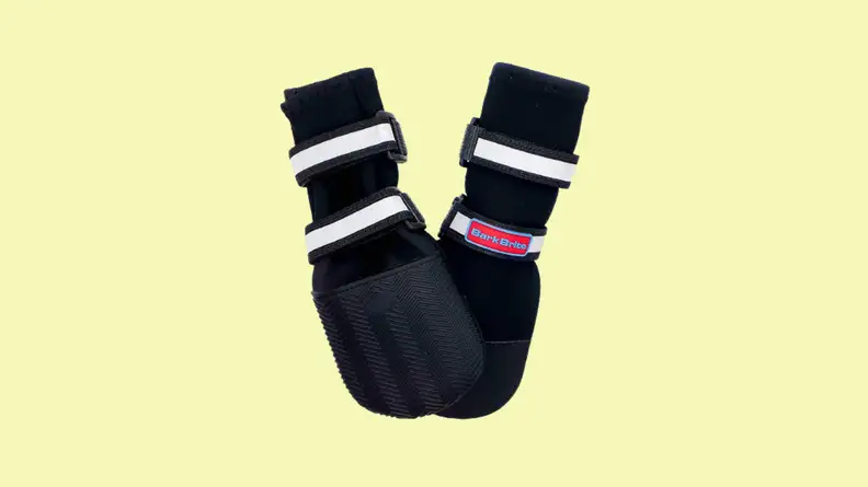 Black and white pair of dog shoes against a yellow background