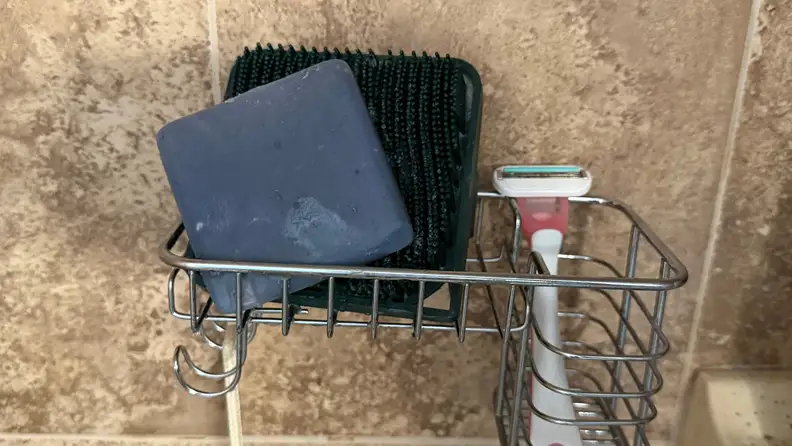 A blue bar of soap rests in a metal holder in a shower