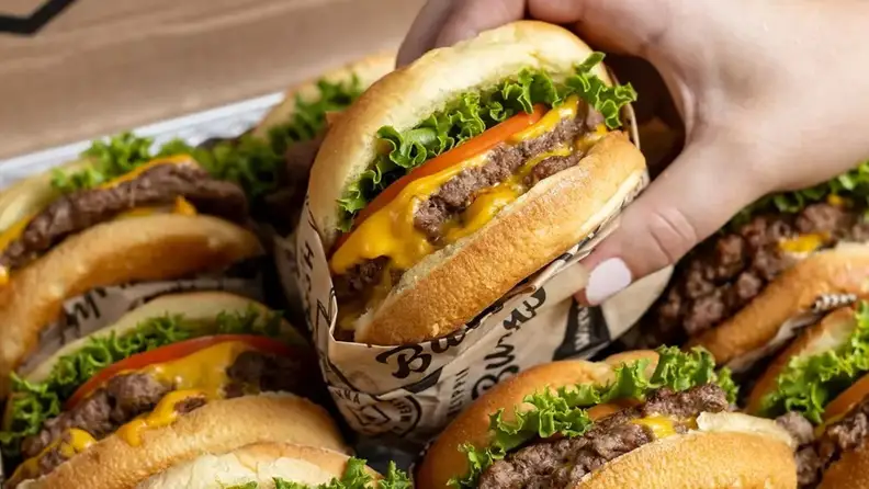 A hand grabbing a cheeseburger from a stack of Wayback burgers