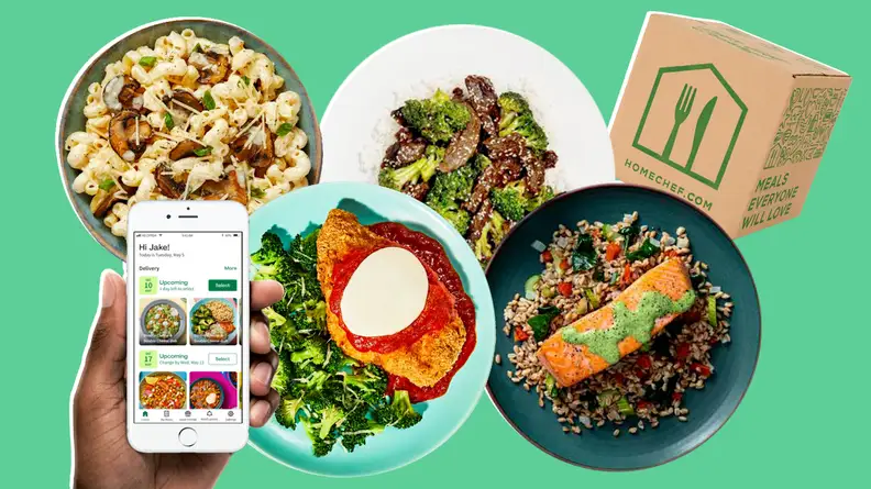 Person holding smart phone with Home Chef app on screen above four plates of cooked meals and delivery box.