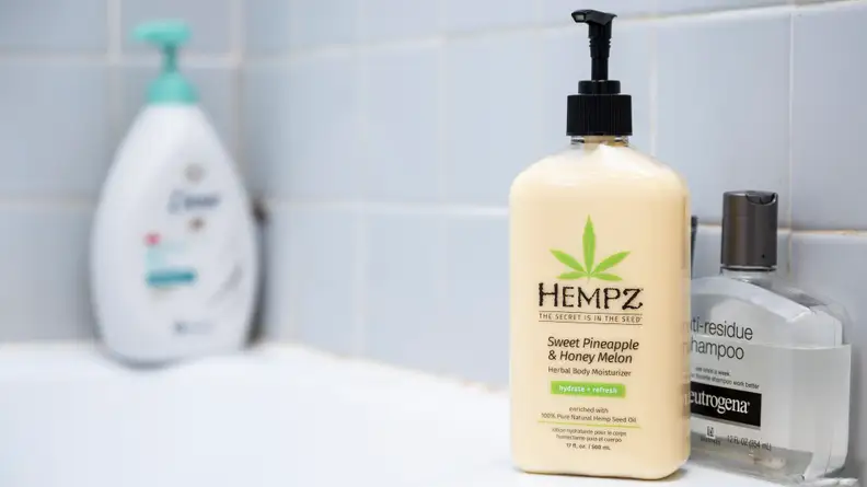 A yellow bottle of Hempz Moisturizing Skin body lotion standing on the side of a tub.