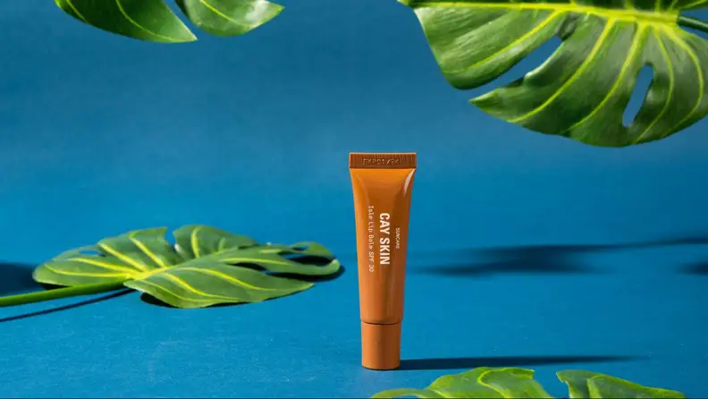 A tube of lip balm against a blue background and foliage.