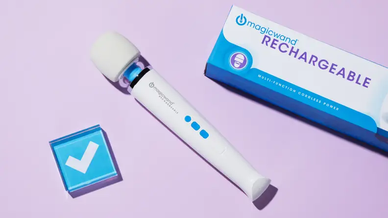 A Wagic Wand Rechargeable rests on a lilac background next to the box it came in and a small paperweight featuring the Reviewed checkmark logo