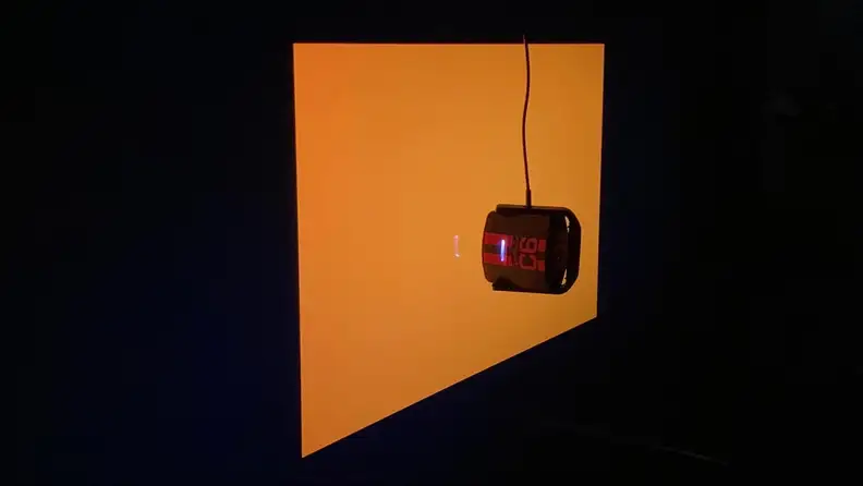 An orange screen at an angle with a device in front of it.