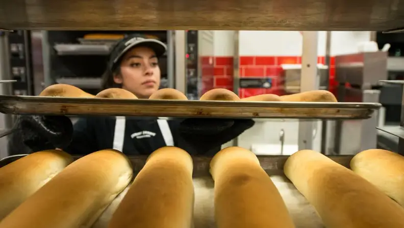 A woman pulling fresh baked bread out of the oven