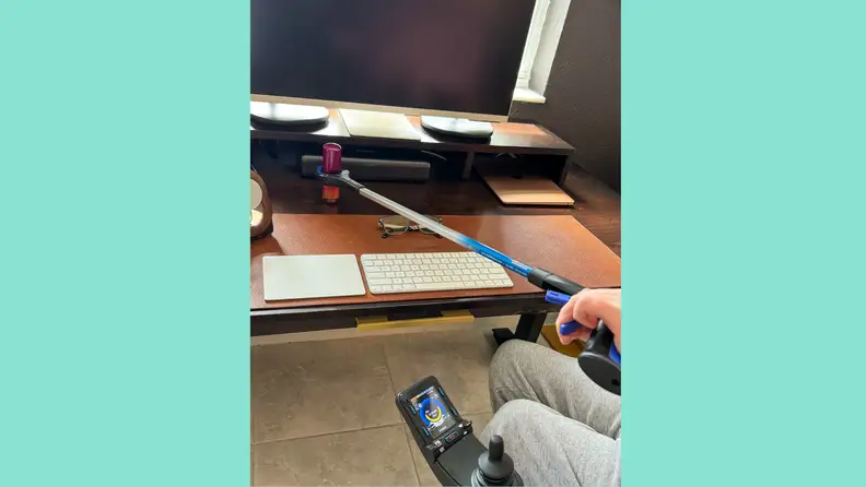 A man in a wheelchair using an RMS reacher grabber to grab a cylinder-shaped object