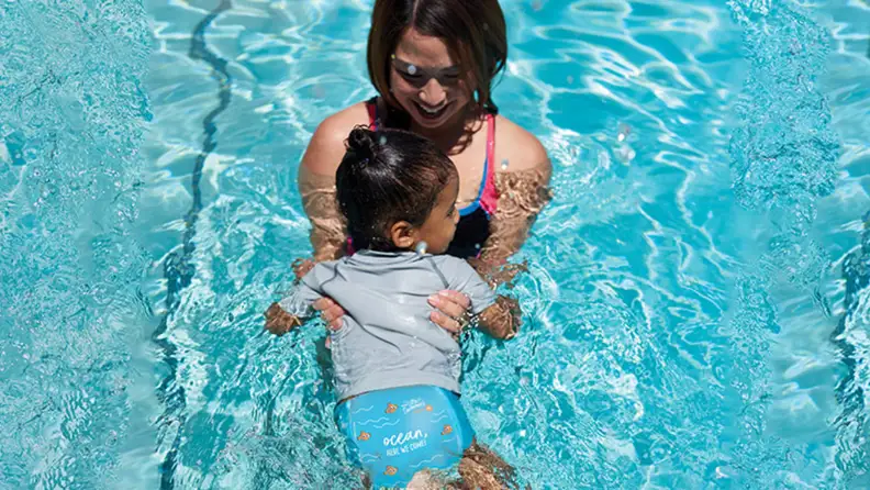 A child wearing a swim diaper in the water with an adult.