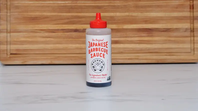 A bottle of Bachan’s Original Japanese Barbecue sauce next to a wood cutting board.