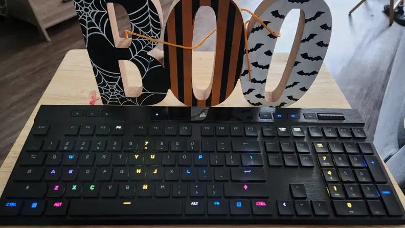 A black keyboard with several keys lit up with different colors and a Halloween 'boo' sign standing behind