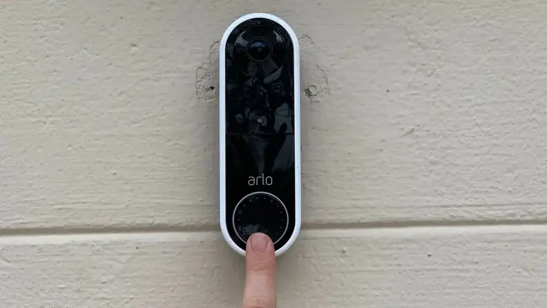 A woman's finger rings the doorbell on the the Arlo Essential Wire-Free Doorbell