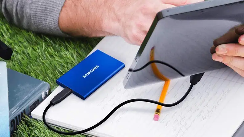 A person uses a tablet with an external hard drive.