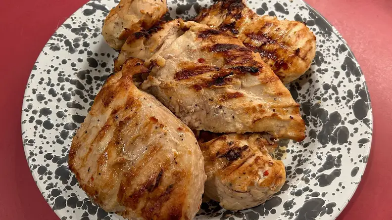 Five seared chicken breasts piled on top of white and black patterned dish sitting on red surface.