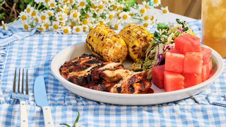 A plate of grilled chicken, corn on the cob, slaw, and watermelon