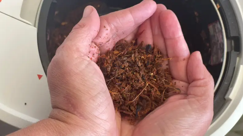 A pair of hands holds dirt made by a Lomi composter.