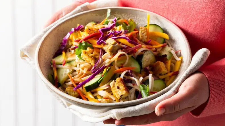 Woman holding noodle bowl.