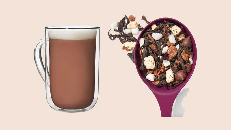 Mug of tea latte and spoon of dried tea leaves on beige background