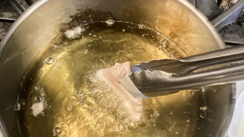 A person uses a pair of tongs to add beer-battered fish to a pot of hot oil.