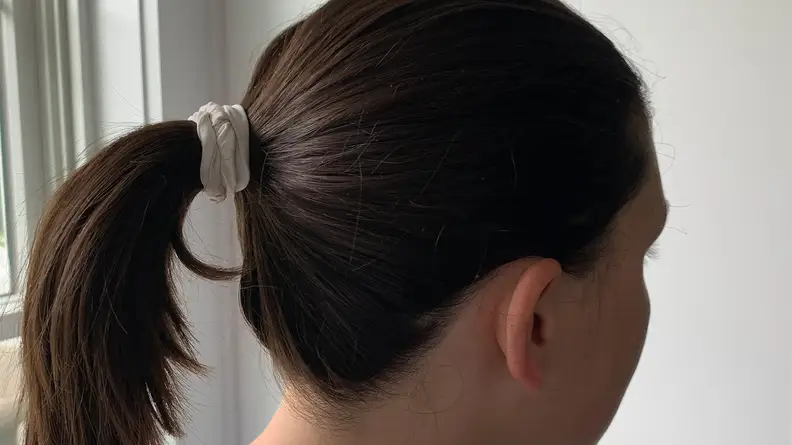 A person with long brunette hair wearing the Lululemon Skinny Scrunchie in her hair for a ponytail.