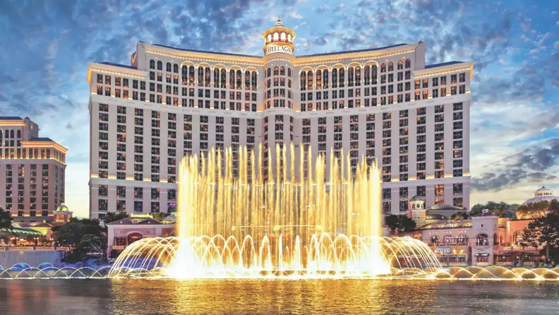 Bellagio Las Vegas with its iconic dancing fountains performing in front of the hotel, illuminated against a colorful evening sky.