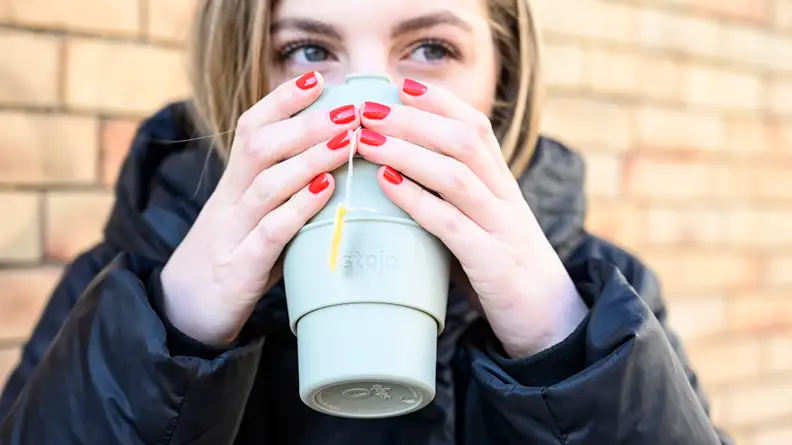 A photo of a woman sipping from the Stojo Cup.