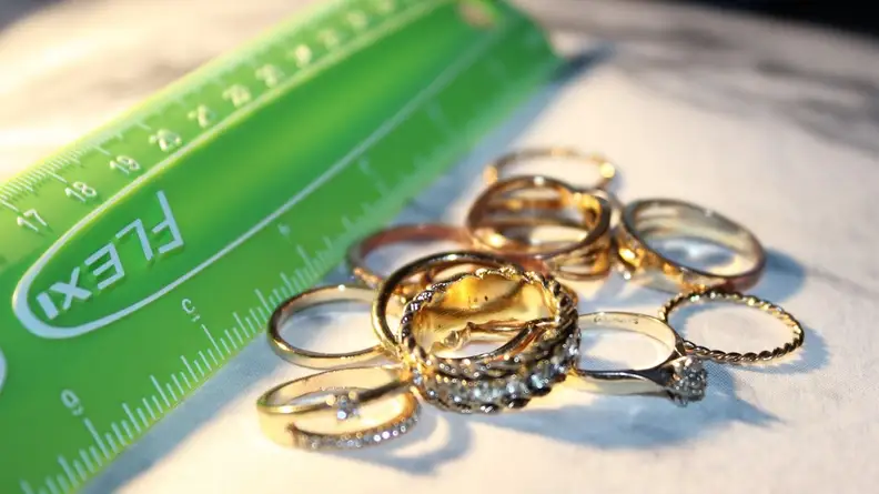 A green ruler propped up next to a stack of gold rings