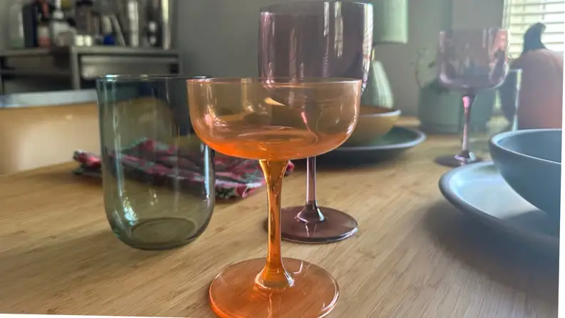 An orange coupe, purple wine glass, and green tumbler on a dining room table.