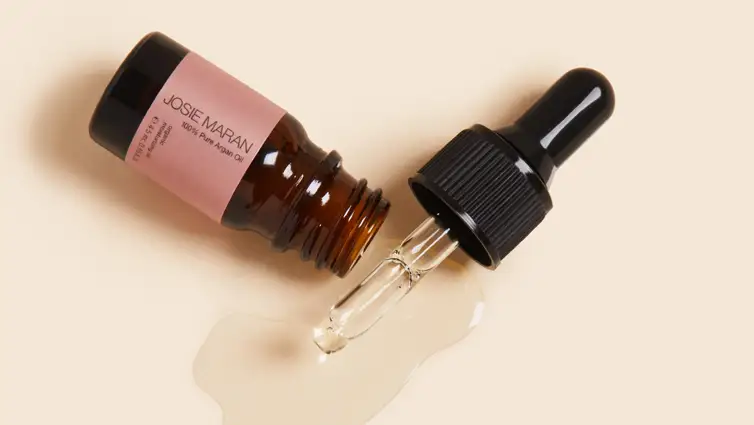 Bottle of argan oil with dropper on beige background