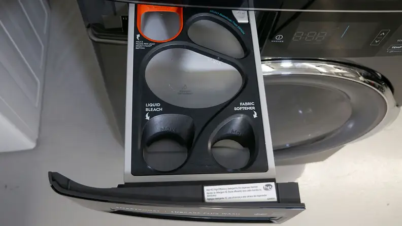 The image shows a pull out detergent tray with room for a laundry pod, fabric softener, bleach, and reservoirs for detergent.