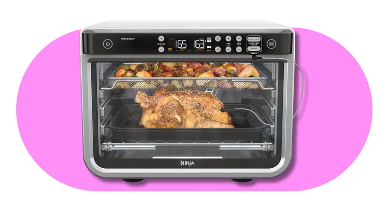 Ninja countertop oven roasting a whole chicken with vegetables inside.