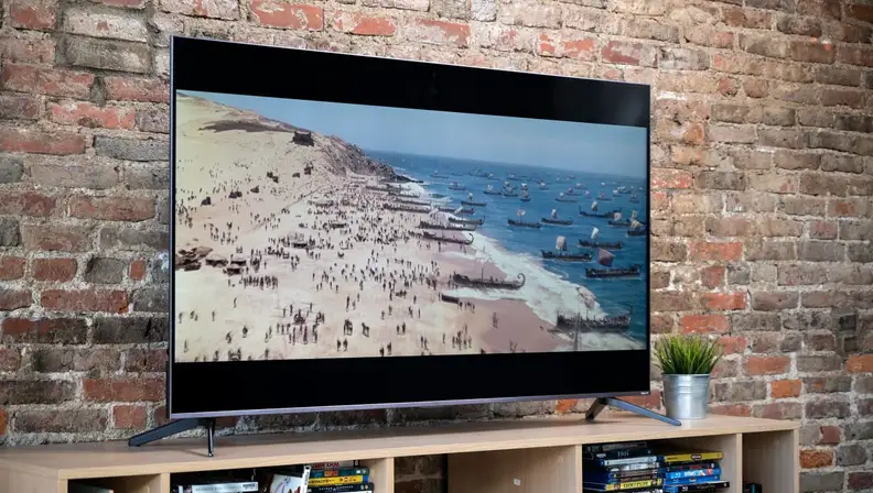 A TCL TV on a media console, showing a scene of a beach war scene.
