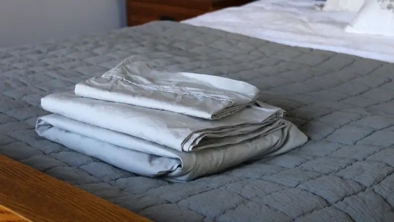 A folded set of percale sheets from Linen Home stacked on the end of a bed.