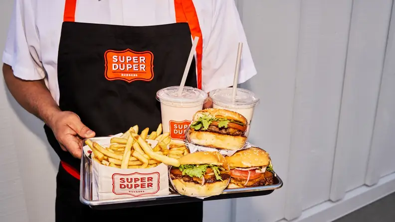 A worker holding a tray of burgers, fries, and shakes from Super Duper