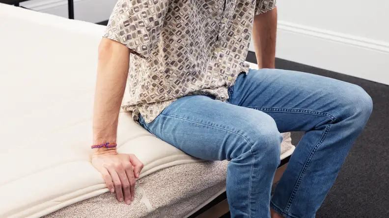 Tester Chris Panella sits at the edge of the Birch Natural Mattress, which has been lauded by customers for its mix of softness and firmness.