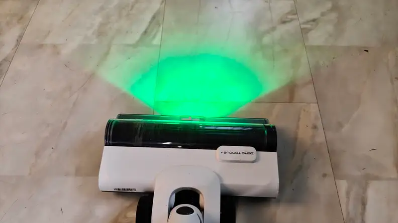 A white vacuum head shines a green light on a beige tile floor