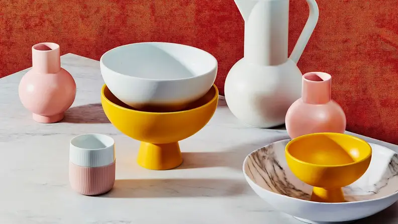 Various pink, white, and marigold yellow ceramic vessels arranged on a white surface.